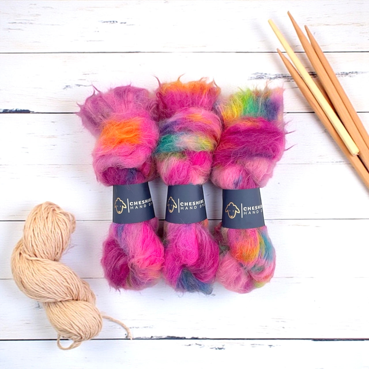 Colorful baby alpaca and merino yarn skeins with wooden knitting needles on a white wooden surface
