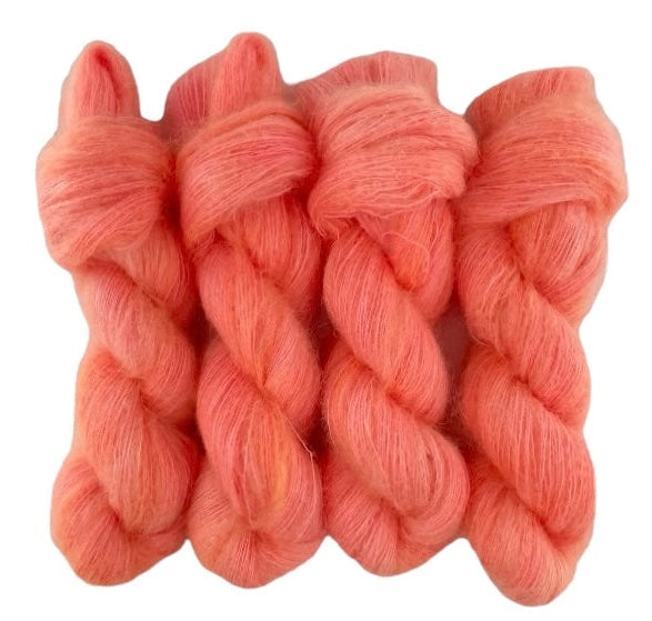 Four orange pink hand dyed skeins of lace weight mohair and silk yarn on a white background.