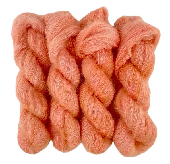 Four pale red orange hand dyed skeins of lace weight mohair and silk yarn on a white background.