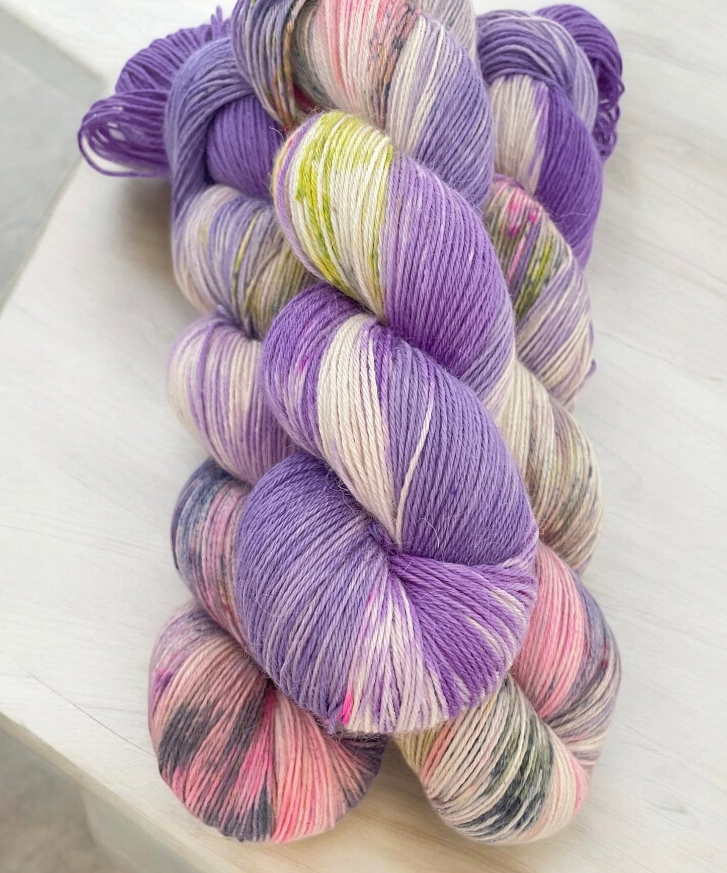 Three skeins of fingering weight baby alpaca, silk and cashmere yarn, hand dyed in shades of purple, pink and yellow.