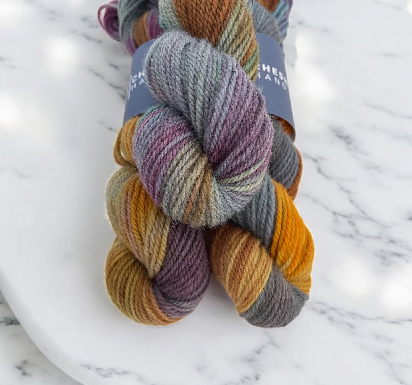 Three skeins of multicolored non superwash DK merino and bluefaced leicester yarn with 'Cheshire Hand Dyed' labels on a marbled surface
