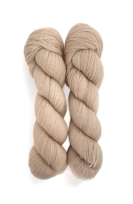 Two skeins of hand-dyed, fingering/sock weight yarn in a beige color, made from 100% Peruvian Highland Wool.