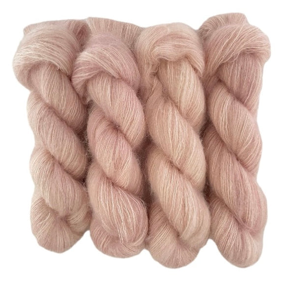 Four beige hand dyed skeins of lace weight mohair and silk yarn on a white background.