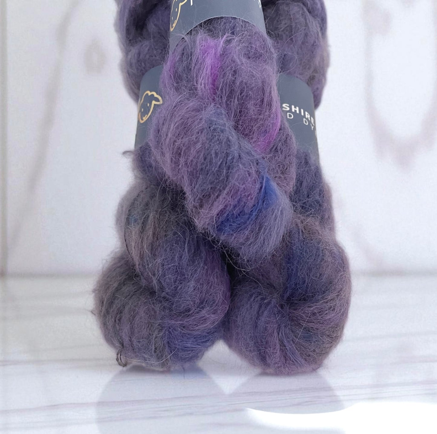 Three skeins of lace weight suri alpaca yarn, hand dyed in shades of purple.