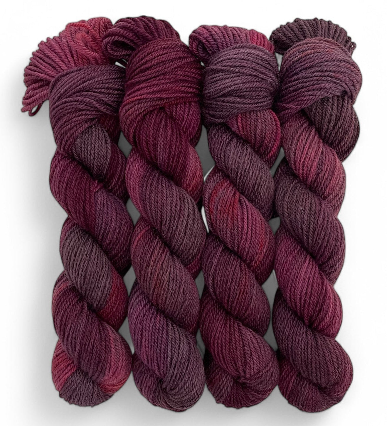 Four red and brown hand dyed 50g skeins of non superwash DK merino and blue faced leicester on a white background.