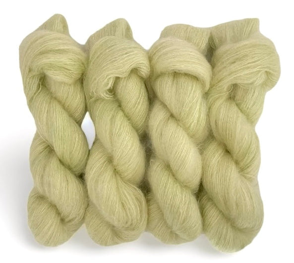 Four pale yellow hand dyed skeins of lace weight mohair and silk yarn on a white background.