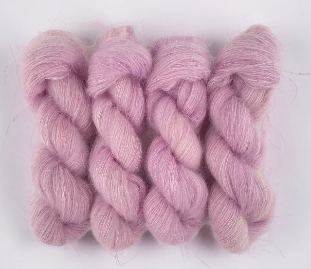 Four pink hand dyed skeins of lace weight mohair and silk yarn on a white background.