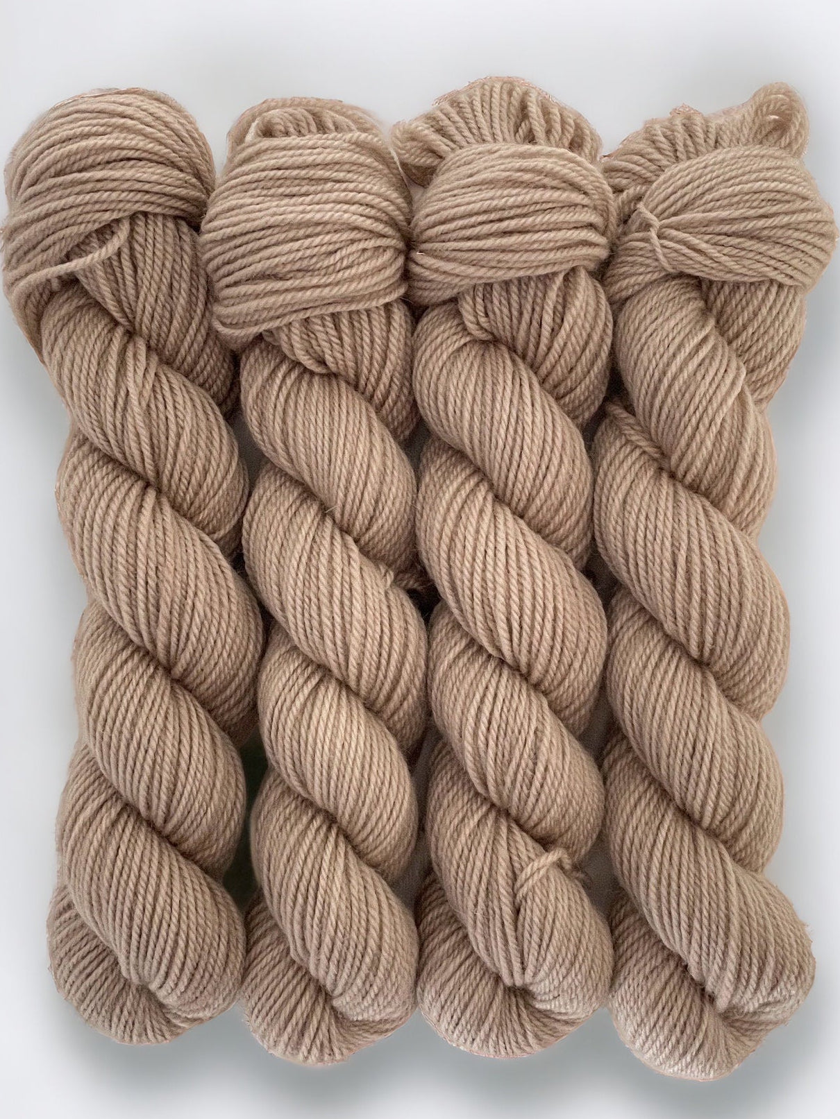 Three skeins of beige merino and blue faced Leicester non-superwash yarn on a white background. Hand dyed. DK