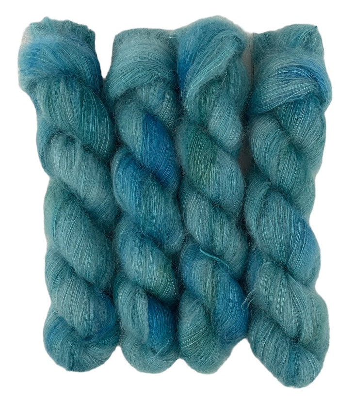Four blue green hand dyed skeins of lace weight mohair and silk yarn on a white background.