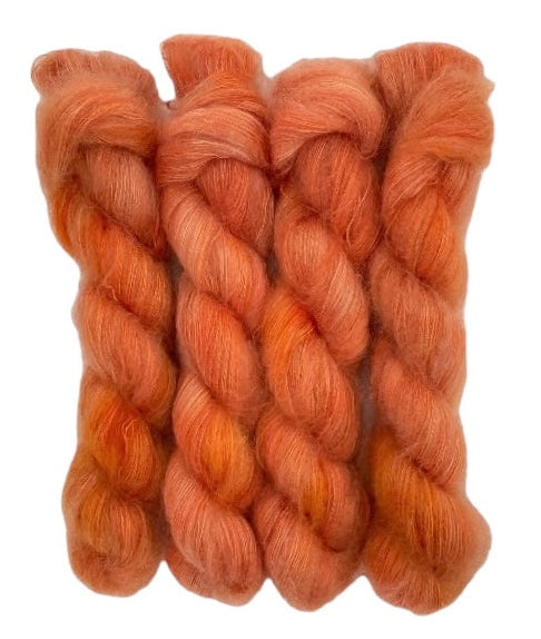 Four orange hand dyed skeins of lace weight mohair and silk yarn on a white background.