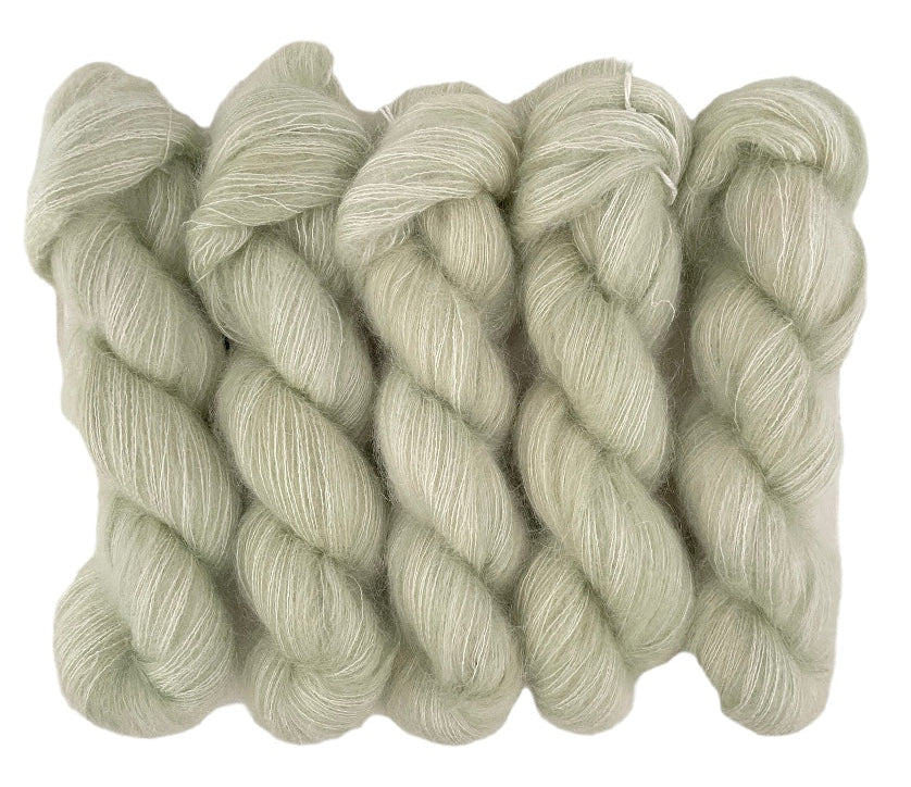 Five pale green hand dyed skeins of lace weight mohair and silk yarn on a white background.