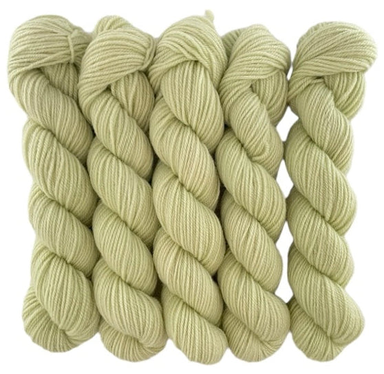 Five skeins of pale green or yellow merino and blue faced Leicester non-superwash yarn on a white background. Hand dyed. DK