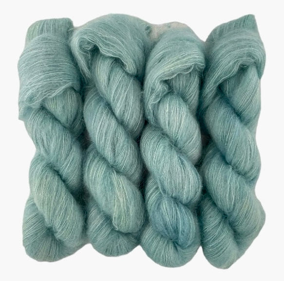 Four blue green hand dyed skeins of lace weight mohair and silk yarn on a white background.