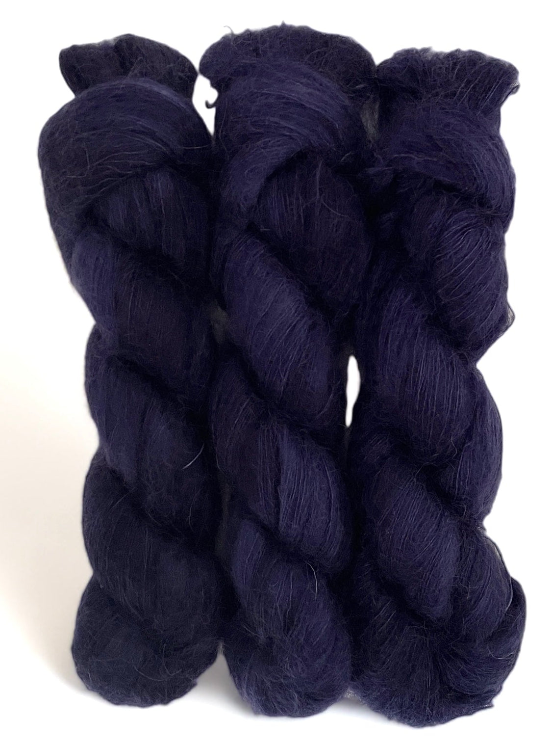 Three dark purple hand dyed skeins of lace weight mohair and silk yarn on a white background.