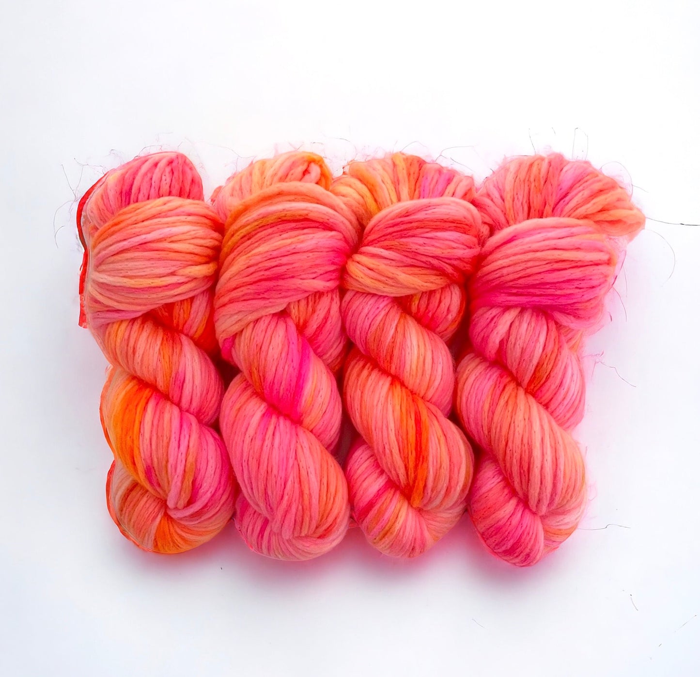 A skein of hand-dyed bright sunshine yarn in pink, orange, and coral colors.
