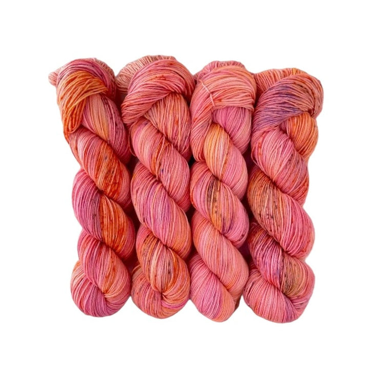 A skein of hand-dyed Tuscan Sunshine yarn in fingering/sock weight, featuring shades of pink, orange, and purple.