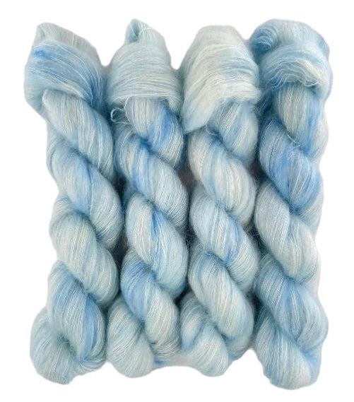 Four pale blue hand dyed skeins of lace weight mohair and silk yarn on a white background.
