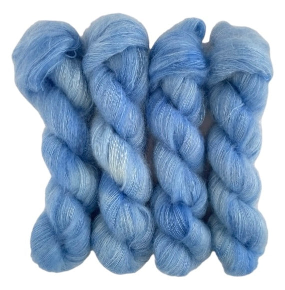 Four pale blue hand dyed skeins of lace weight mohair and silk yarn on a white background.