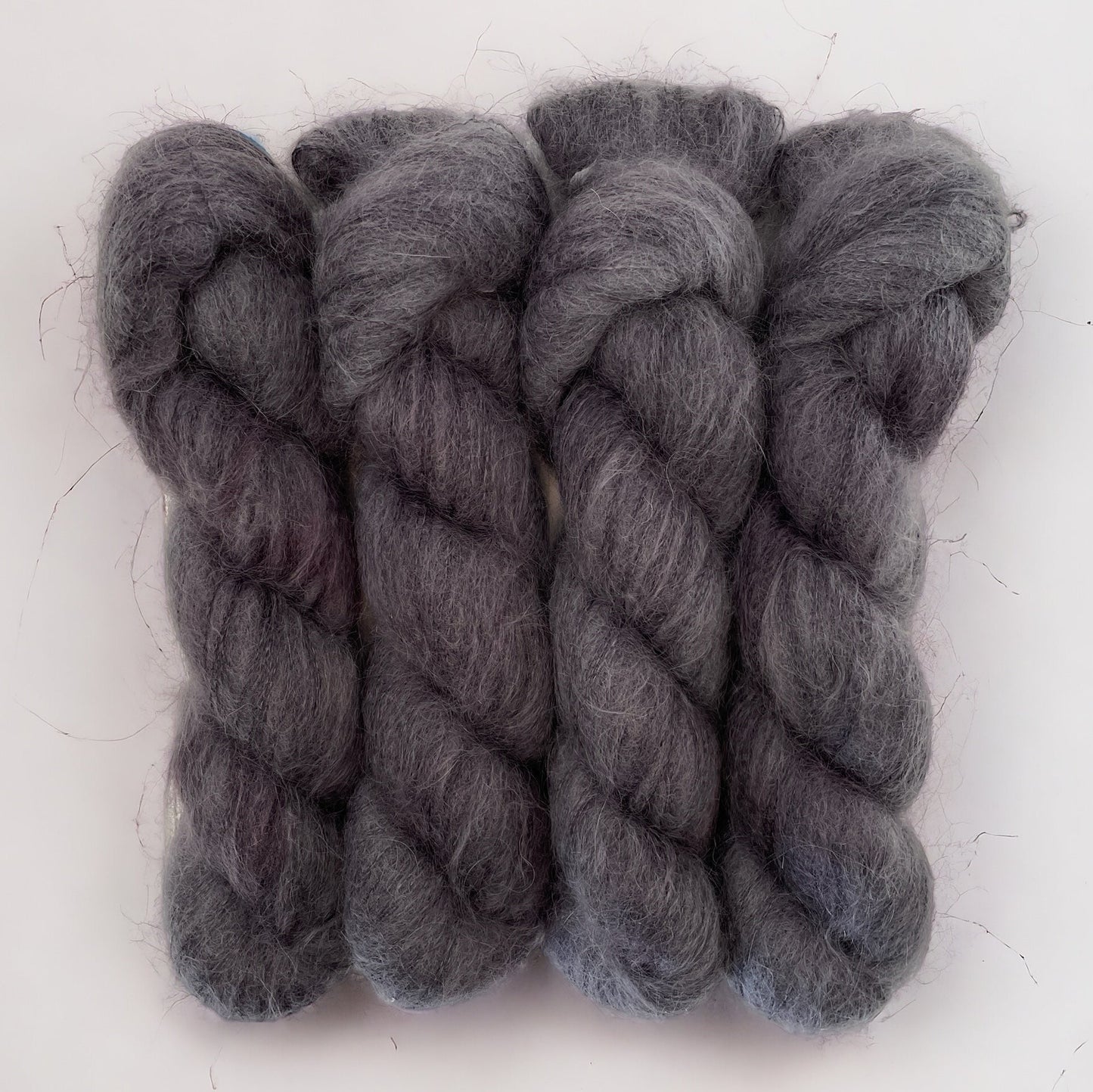 Four grey hand dyed skeins of lace weight mohair and silk yarn on a white background.