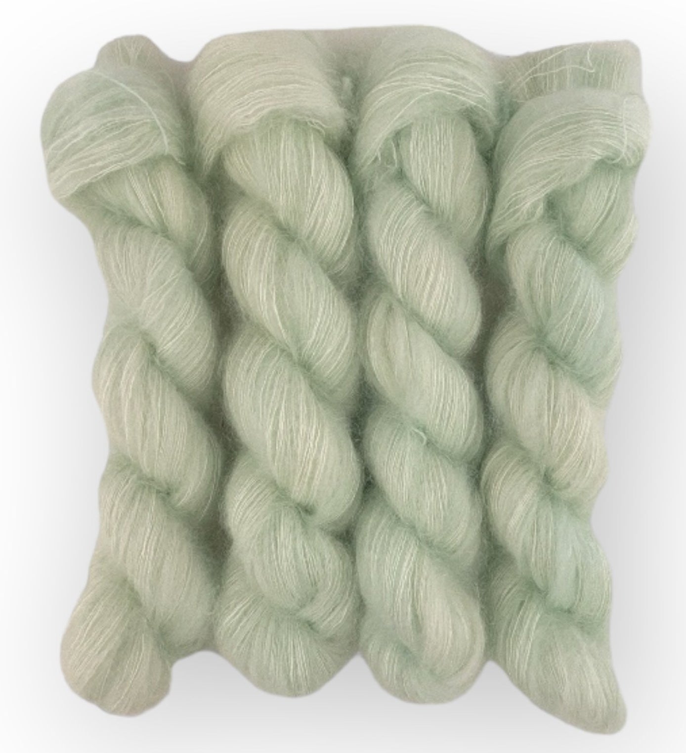 Four pale green hand dyed skeins of lace weight mohair and silk yarn on a white background.