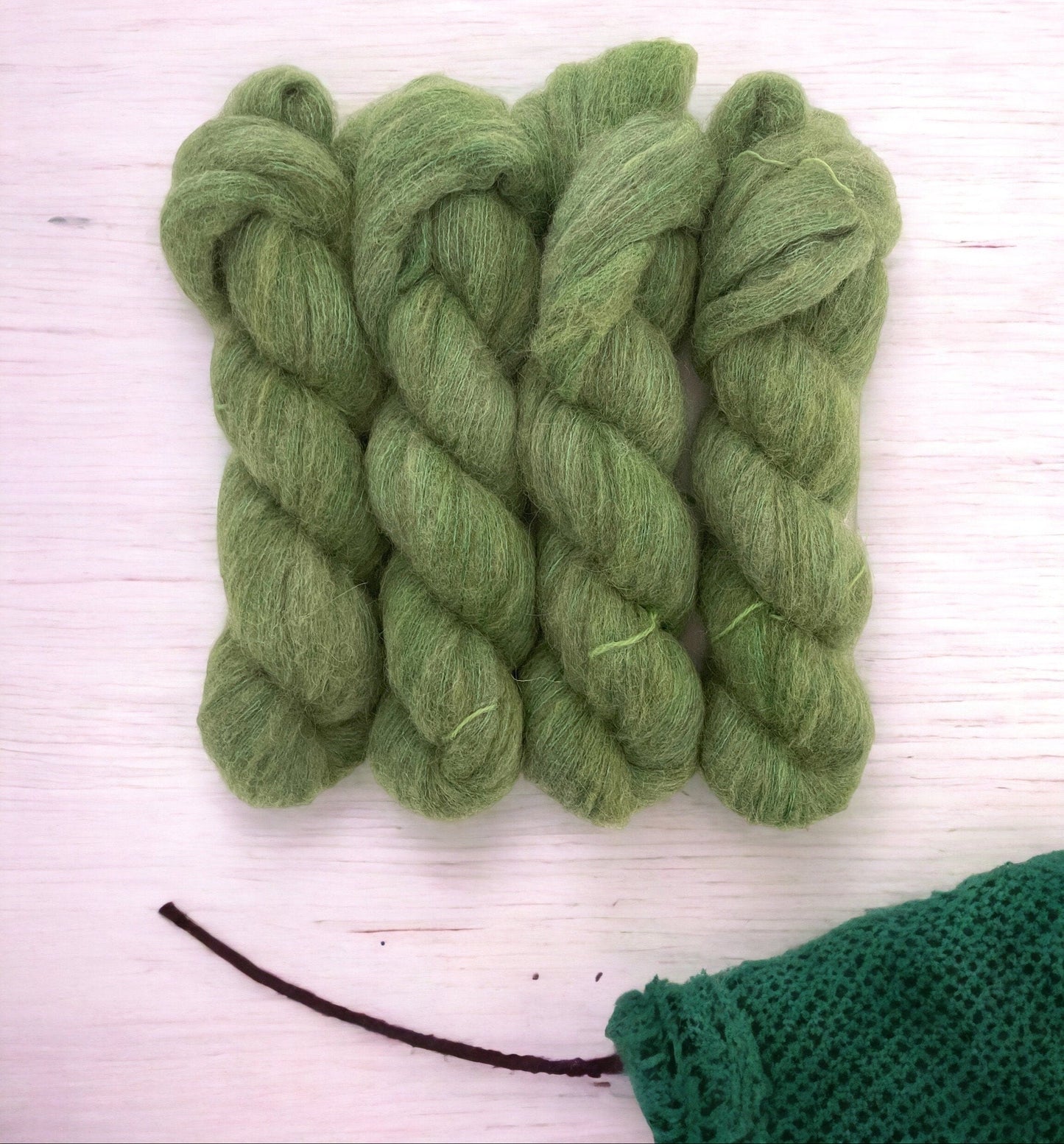 Four skeins of hand-dyed, lace weight yarn in green color, made from a blend of baby alpaca, mulberry silk, fine merino, and yak.