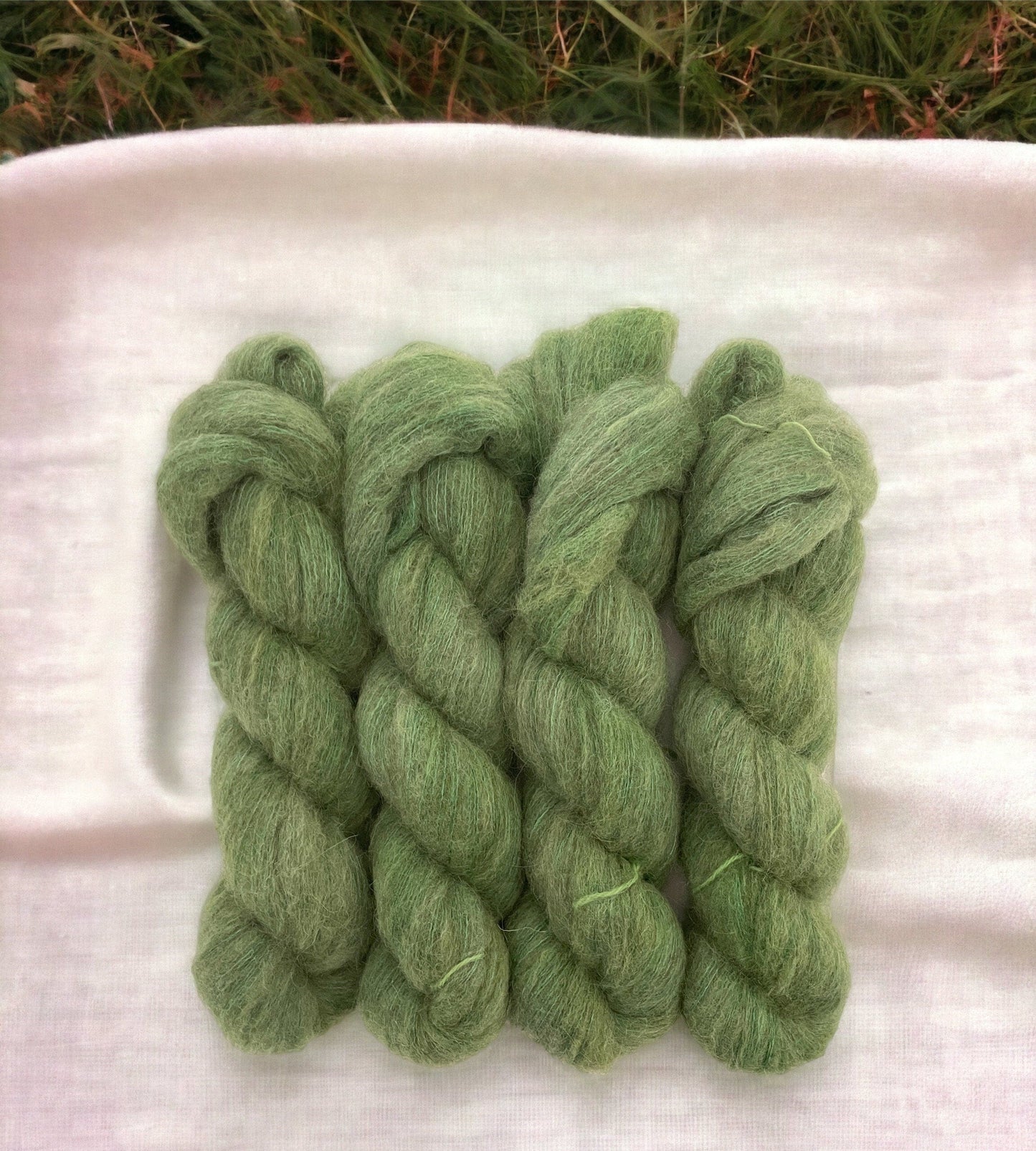 Four skeins of hand-dyed, lace weight yarn in green color, made from a blend of baby alpaca, mulberry silk, fine merino, and yak.