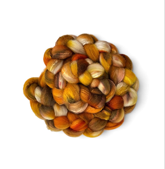 A small pile of variegated mohair wool roving with blended shades of orange, yellow, brown, and cream, photographed from directly above on a white background.