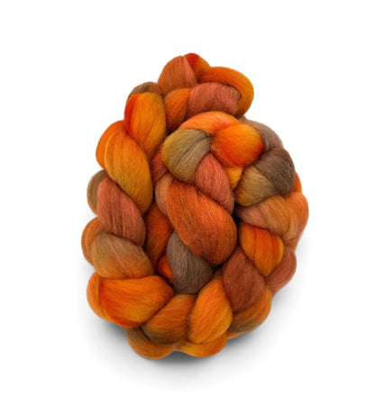 A coiled bundle of soft, twisted wool fibers in a warm autumn colorway, featuring shades of orange, rust, golden yellow, and brown, isolated on a white background.