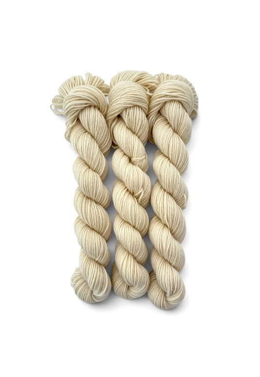 Three skeins of cream-colored yarn twisted into plies, arranged vertically on a clean white background.