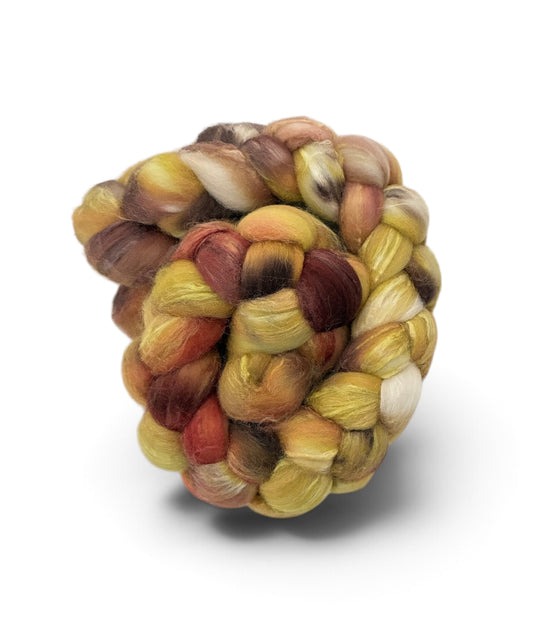 A coiled bundle of variegated wool roving or fiber, featuring a mix of golden yellow, light brown, reddish-brown, and cream colors, set against a plain white background.