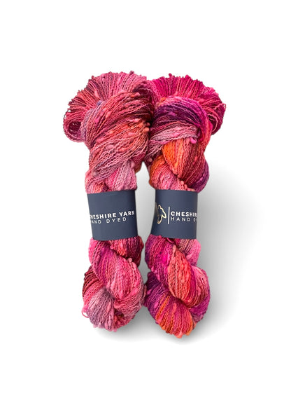 Two skeins of multi-coloured orange and red hand-dyed Cheshire Yarn, Fingering weight Slub yarn made of SW Merino and Nylon on a white background