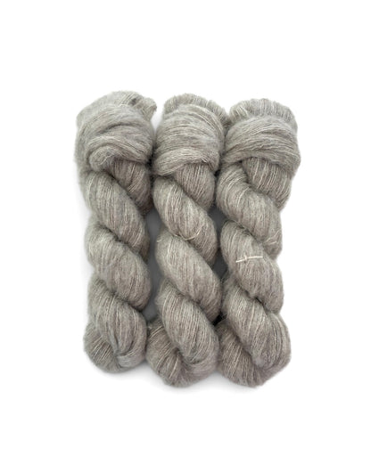 Three skeins of heathered light gray wool yarn arranged side by side on a plain white background.