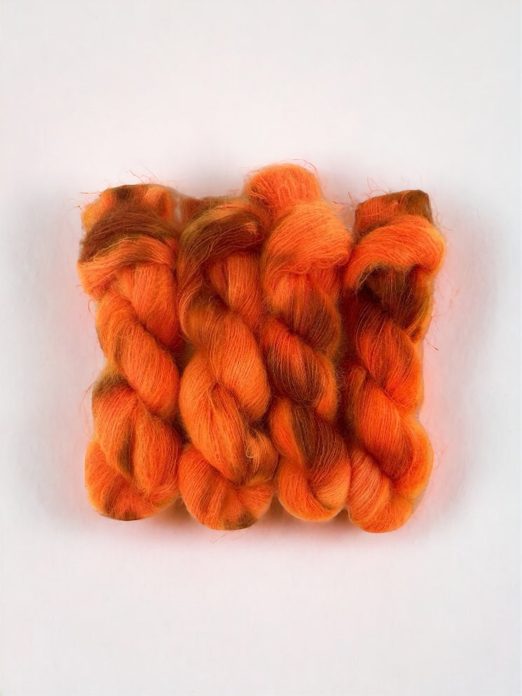 This lace weight yarn blends superkid mohair and silk in a vibrant, bright orange hue with hints of brown. Each 50g skein is hand-dyed for a unique and luxurious touch to your knitting projects.