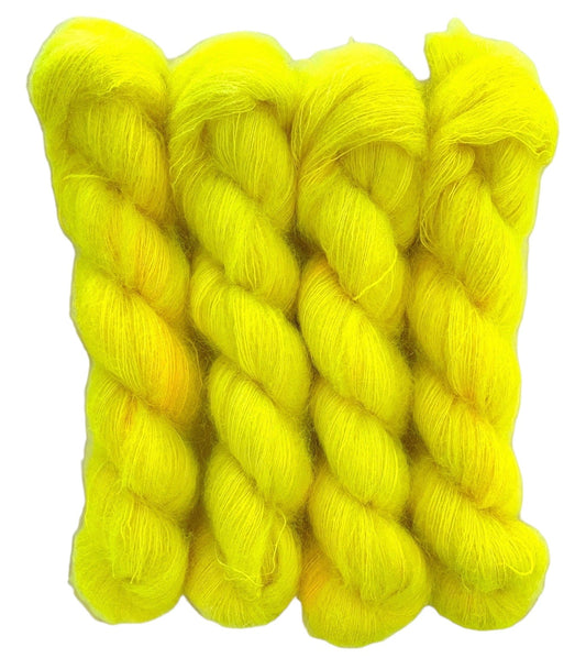 Four yellow hand dyed skeins of lace weight mohair and silk yarn on a white background.