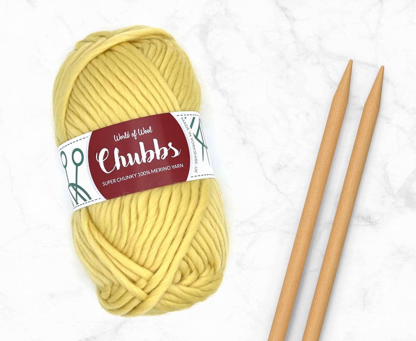 Yellow yarn ball of super chunky 100% merino wool with World of Wool 'Chubbs' label and wooden knitting needles on a white background