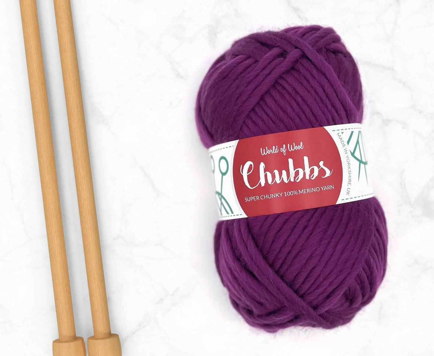 Purple yarn ball of super chunky 100% merino wool with World of Wool 'Chubbs' label and wooden knitting needles on a white background