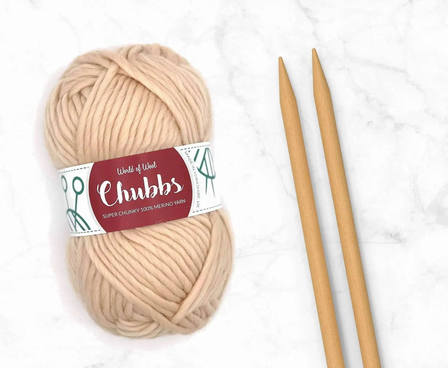 Beige yarn ball of super chunky 100% merino wool with World of Wool 'Chubbs' label and wooden knitting needles on a white background