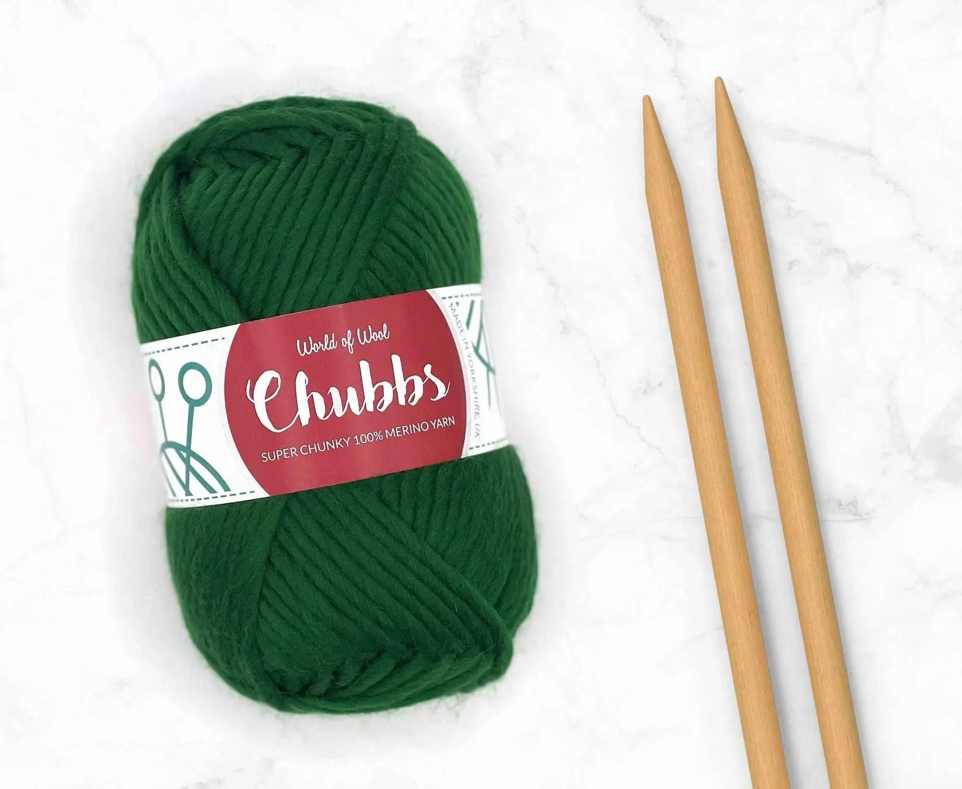 Green yarn ball of super chunky 100% merino wool with World of Wool 'Chubbs' label and wooden knitting needles on a white background