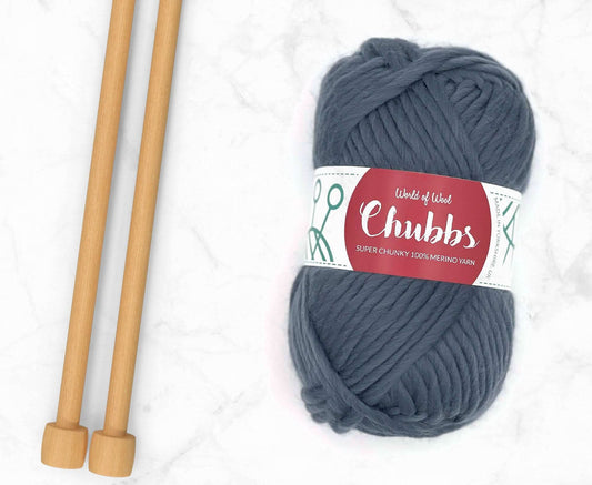 Gray yarn ball of super chunky 100% merino wool with World of Wool 'Chubbs' label and wooden knitting needles on a white background