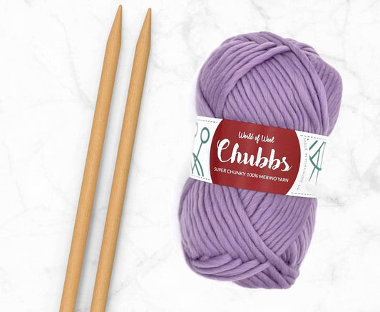Purple yarn ball of super chunky 100% merino wool with World of Wool 'Chubbs' label and wooden knitting needles on a white background