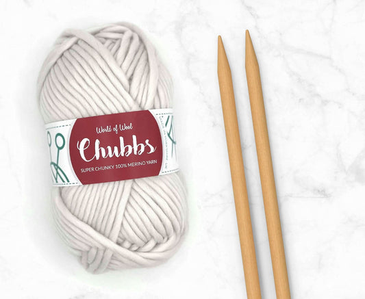 White yarn ball of super chunky 100% merino wool with World of Wool 'Chubbs' label and wooden knitting needles on a white background