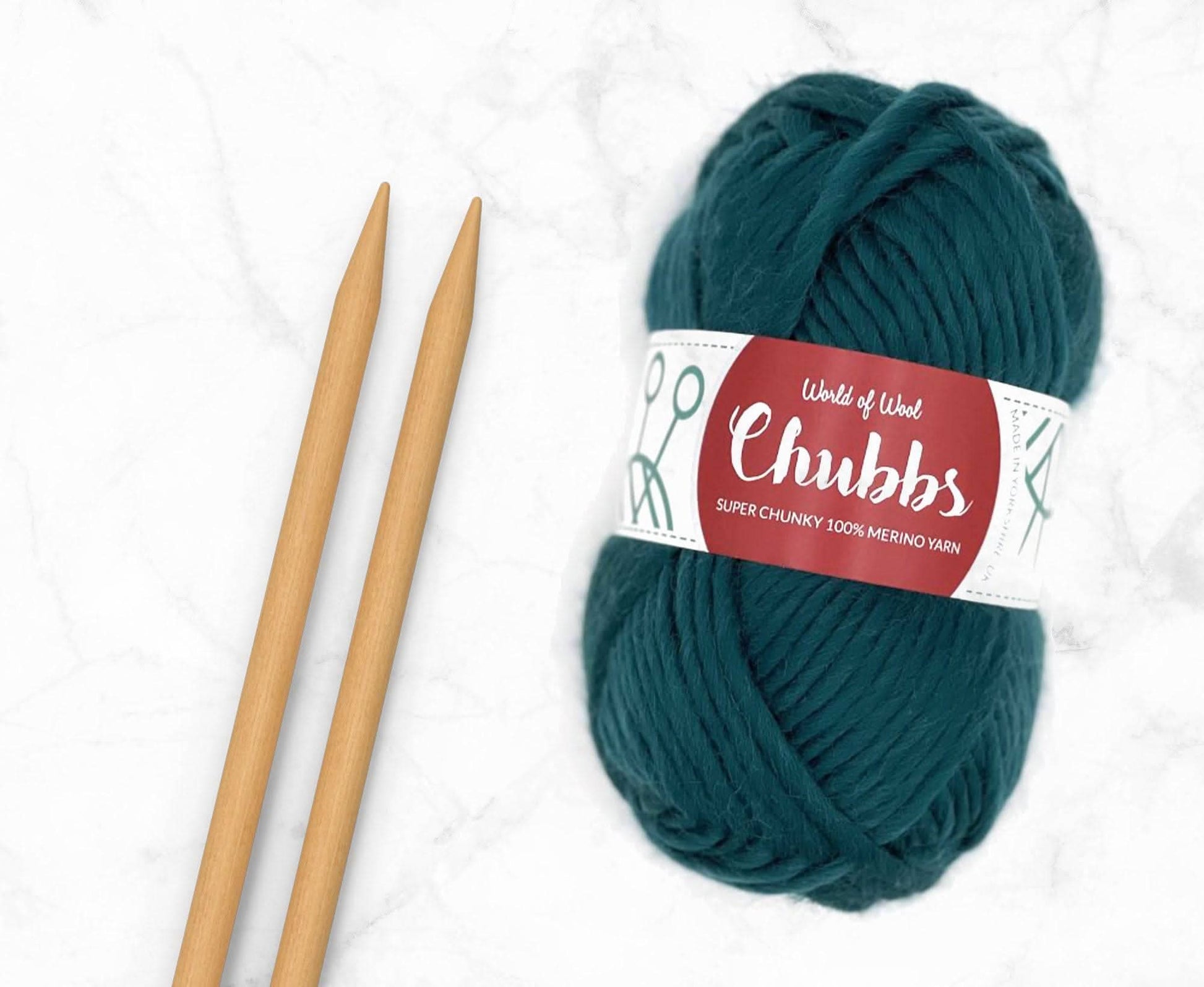 Teal yarn ball of super chunky 100% merino wool with World of Wool 'Chubbs' label and wooden knitting needles on a white background