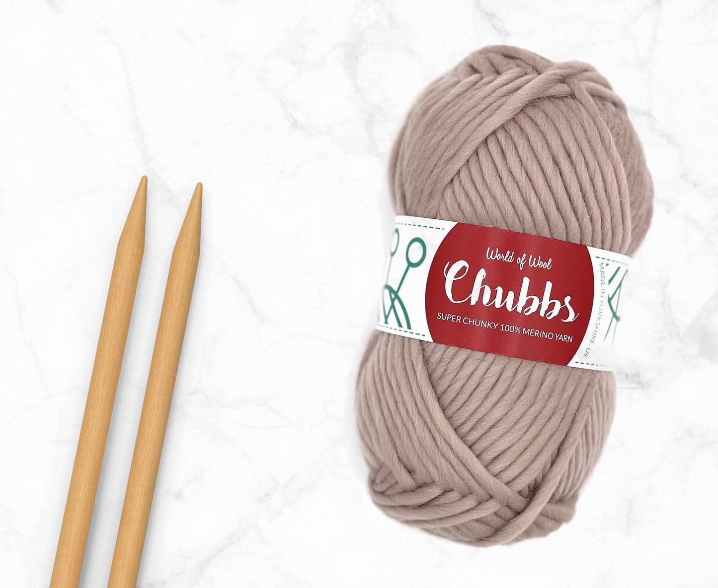 Beige yarn ball of super chunky 100% merino wool with World of Wool 'Chubbs' label and wooden knitting needles on a white background