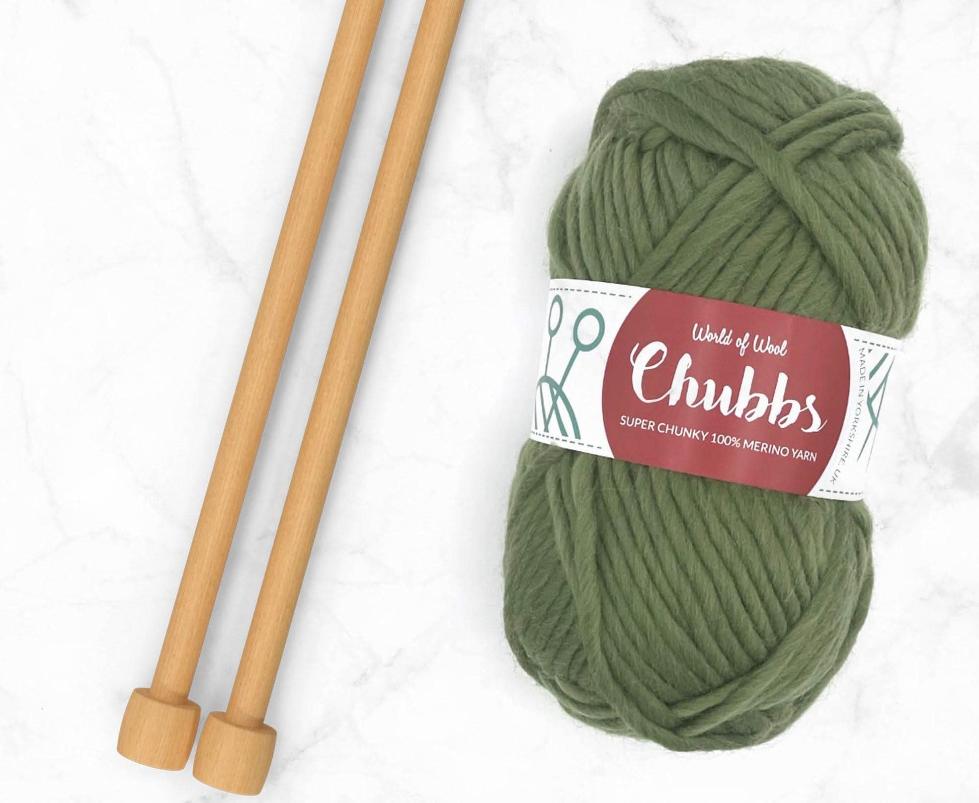 Green yarn ball of super chunky 100% merino wool with World of Wool 'Chubbs' label and wooden knitting needles on a white background