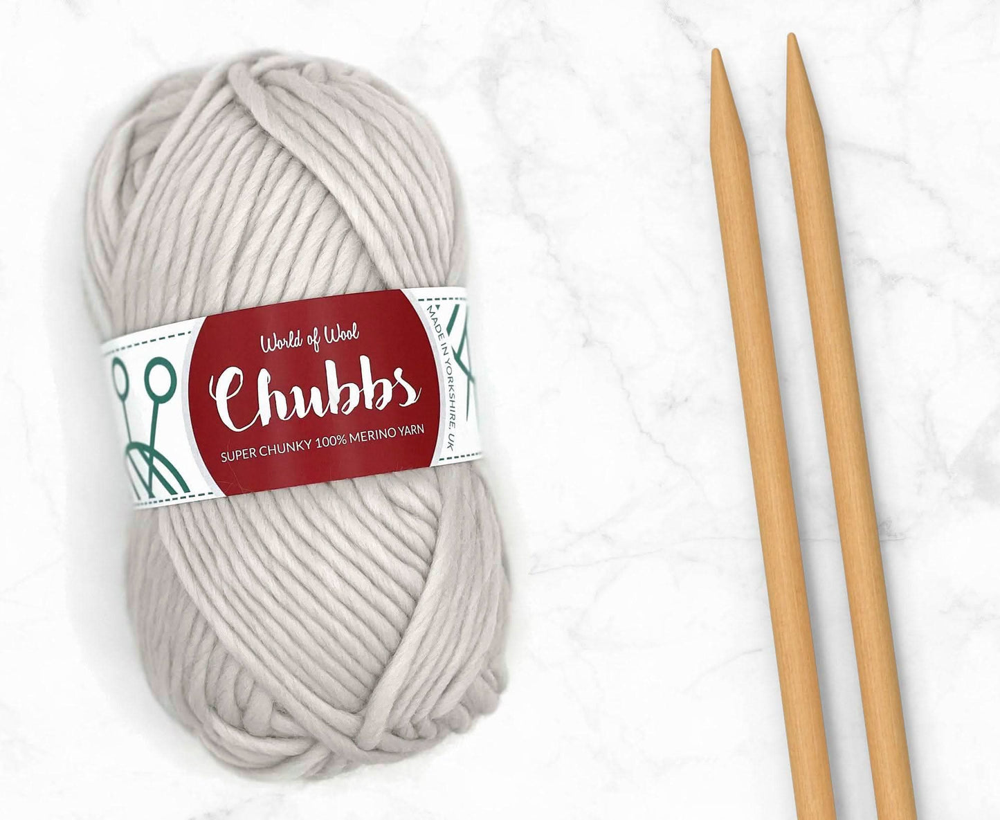 White yarn ball of super chunky 100% merino wool with World of Wool 'Chubbs' label and wooden knitting needles on a white background