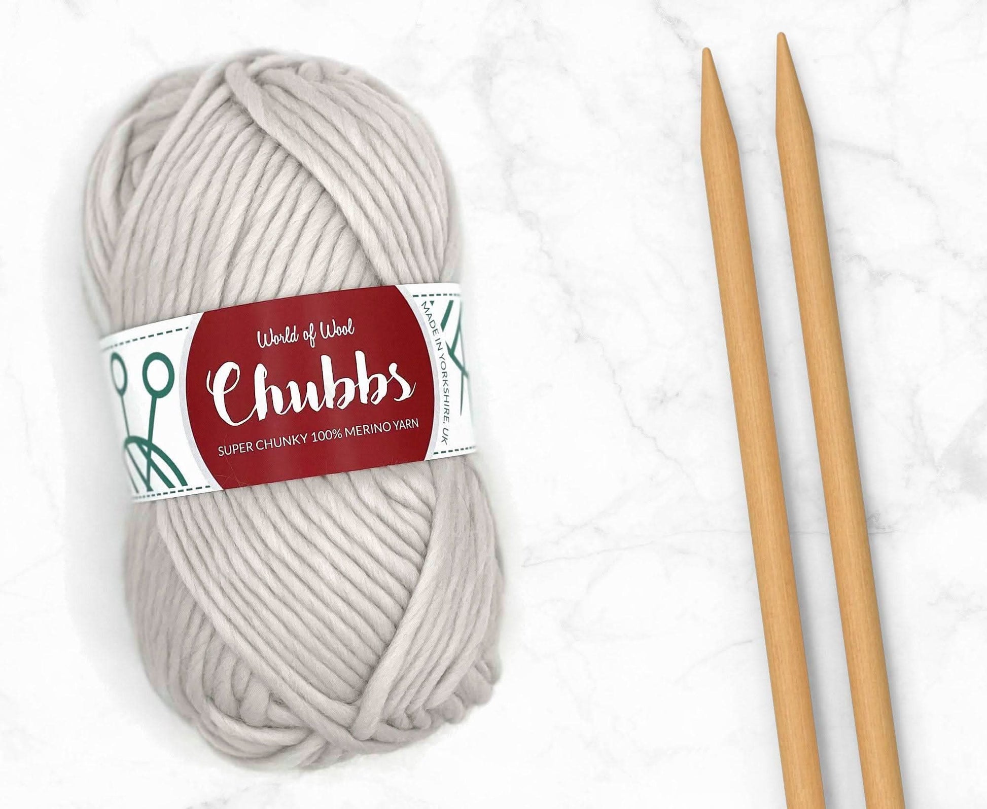 White yarn ball of super chunky 100% merino wool with World of Wool 'Chubbs' label and wooden knitting needles on a white background