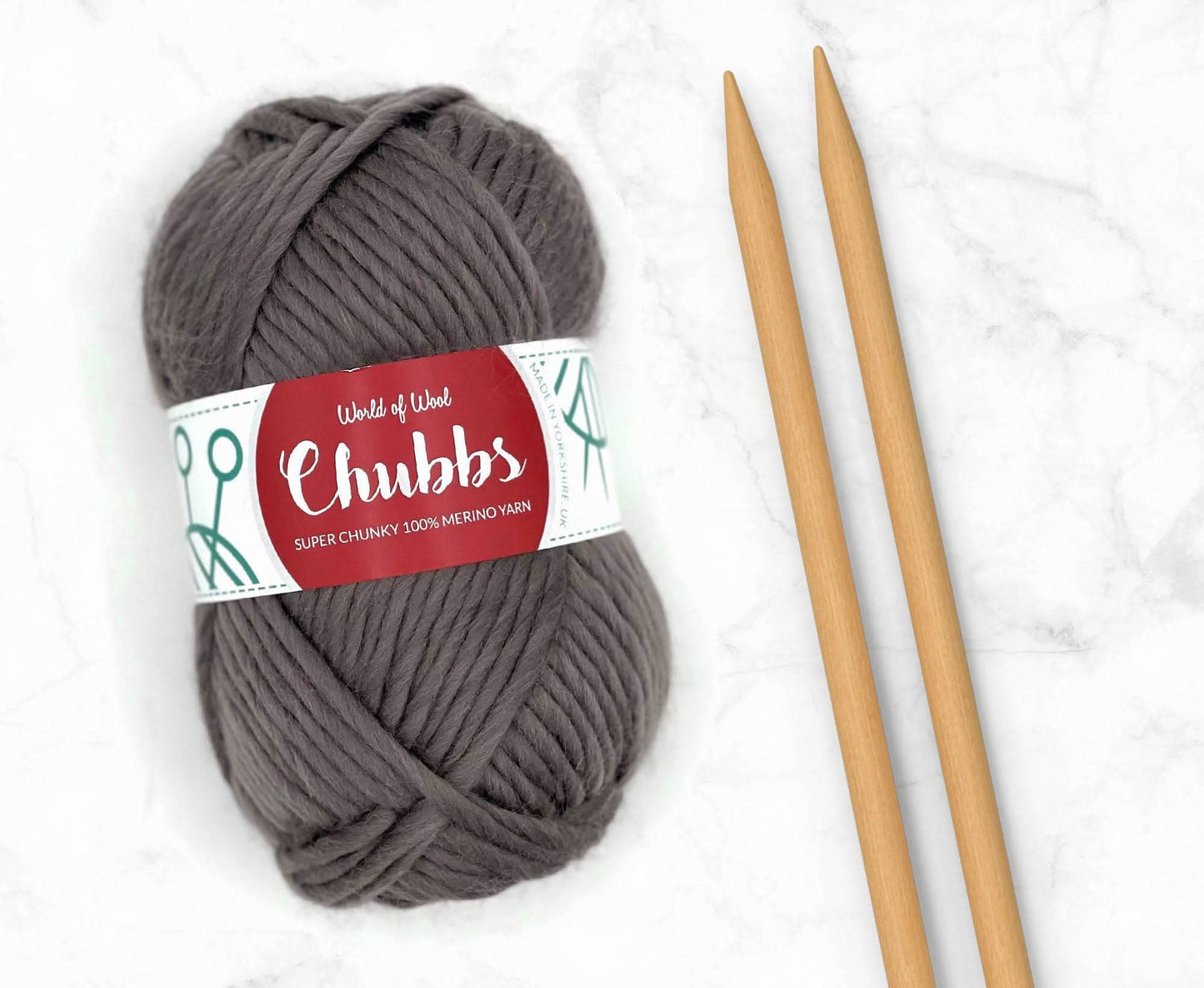 Gray yarn ball of super chunky 100% merino wool with World of Wool 'Chubbs' label and wooden knitting needles on a white background
