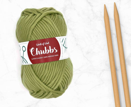 Green yarn ball of super chunky 100% merino wool with World of Wool 'Chubbs' label and wooden knitting needles on a white background