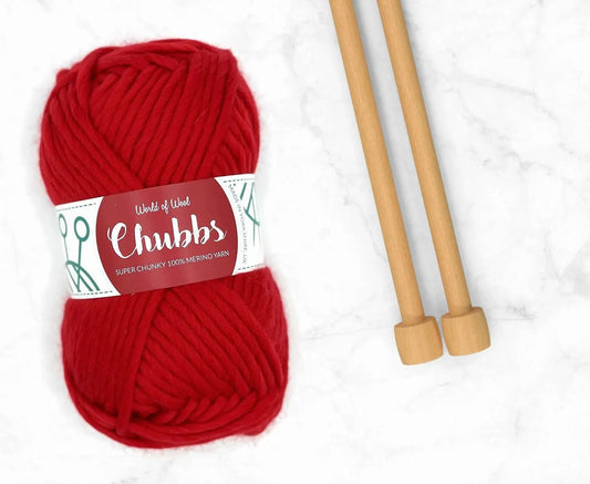 Red yarn ball of super chunky 100% merino wool with World of Wool 'Chubbs' label and wooden knitting needles on a white background