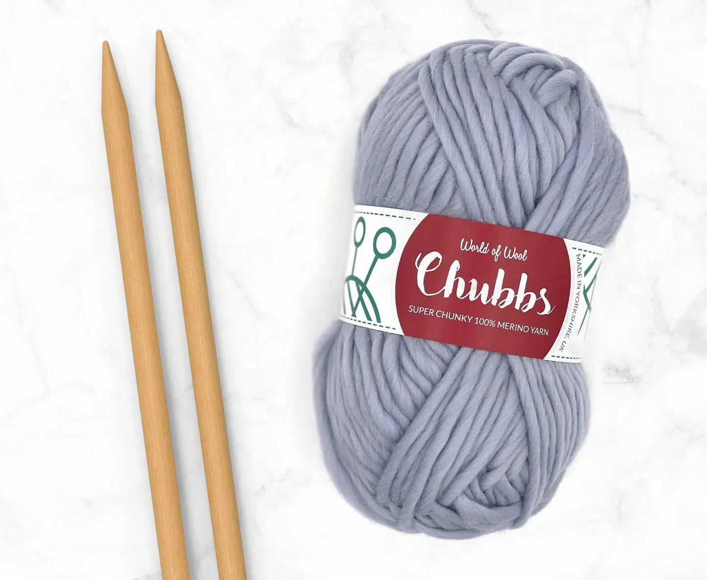 Gray yarn ball of super chunky 100% merino wool with World of Wool 'Chubbs' label and wooden knitting needles on a white background